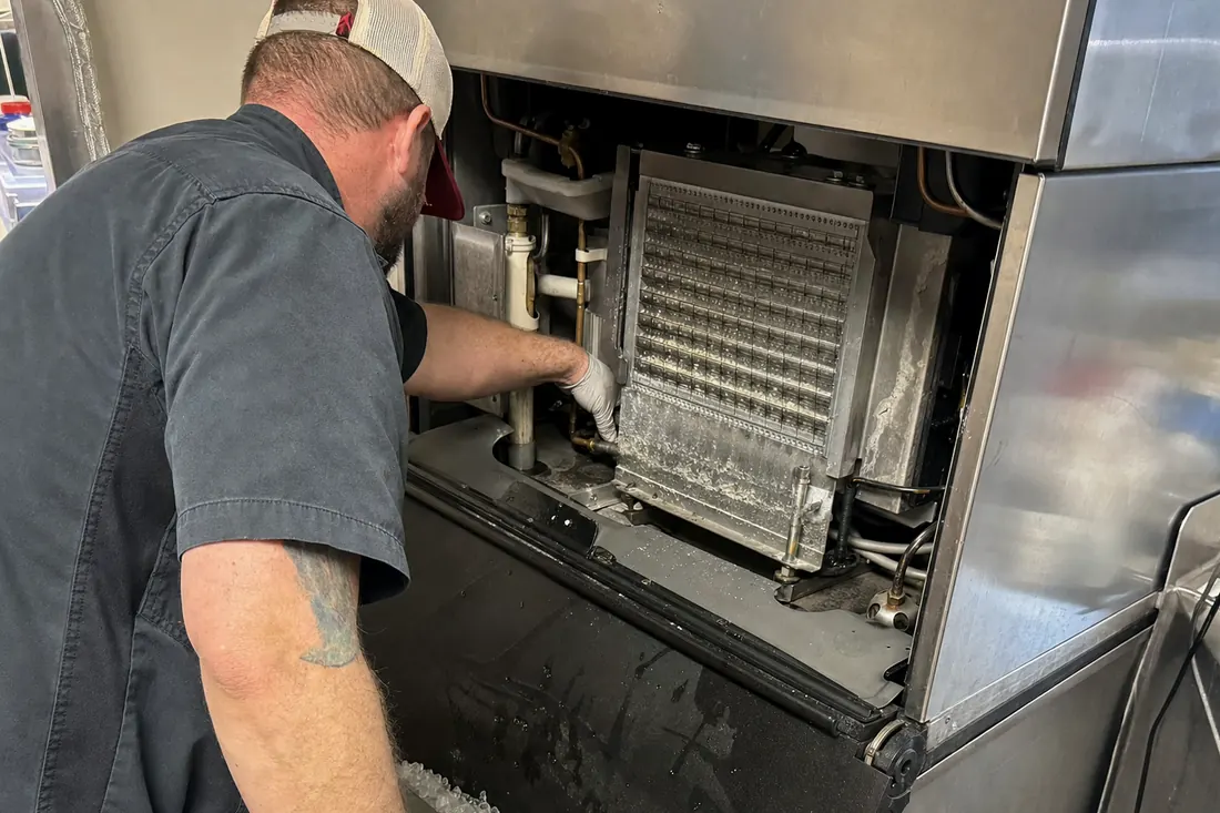 Technician at a stainless ice machine with the top panel off, checking the water line and the evaporator plate, mineral scale on the metal in frame - Questions, answered in order