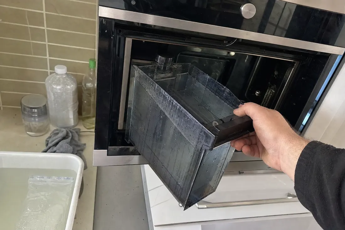 Hands lifting the water reservoir out of a built-in steam oven, the water reservoir in frame - Bosch appliance repair