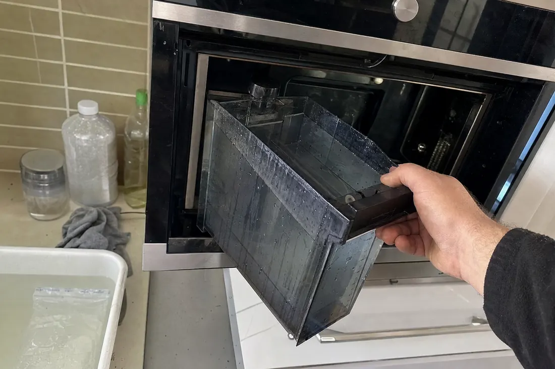 Hands lifting the water reservoir out of a built-in steam oven, the reservoir bay in frame - Built-in dishwasher repair