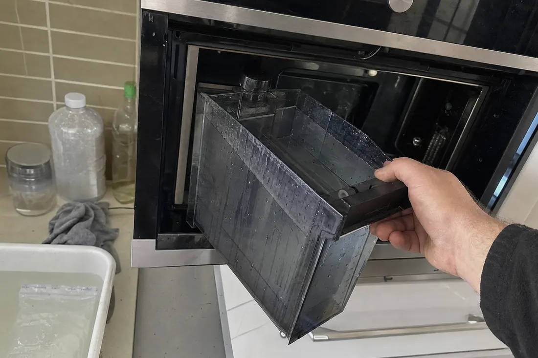 Hands lifting the water reservoir out of a built-in steam oven, the countertop in frame - Humidity, condensation and door gaskets
