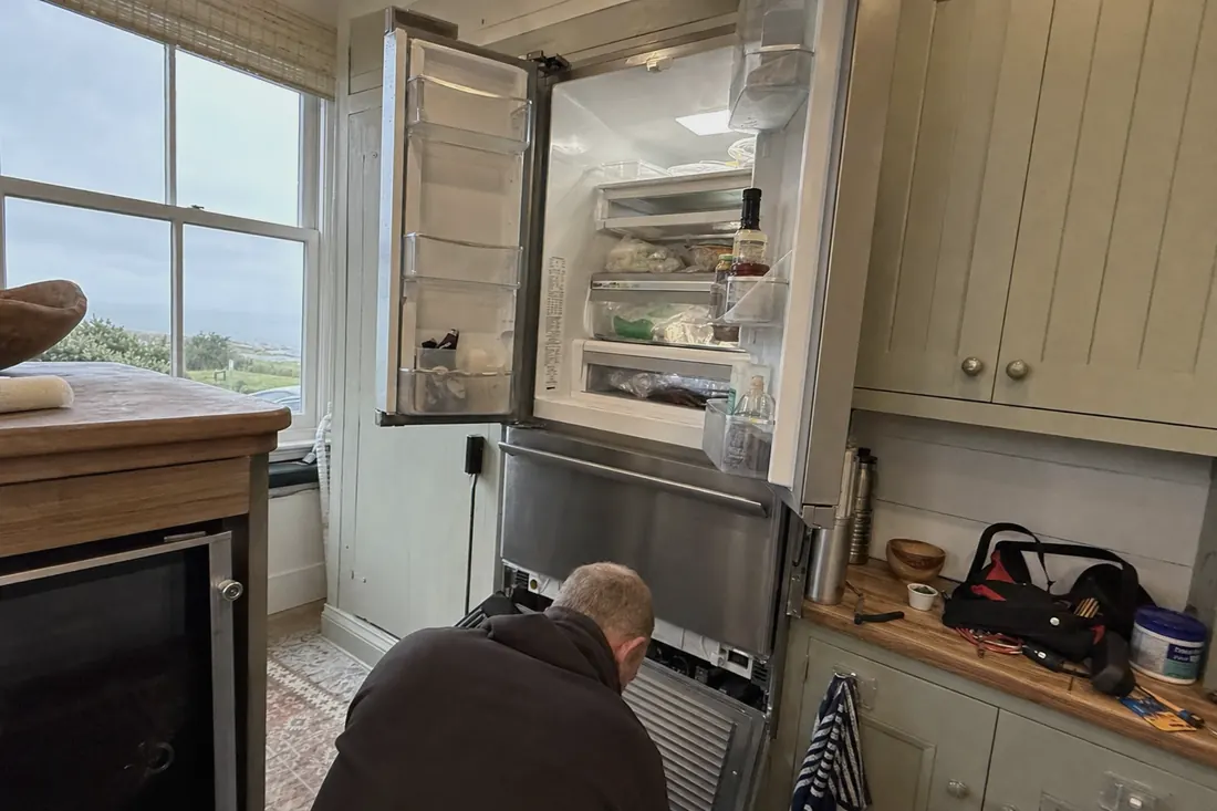 An open built-in refrigerator in a coastal kitchen, technician at the lower grille - An independent shop, by design