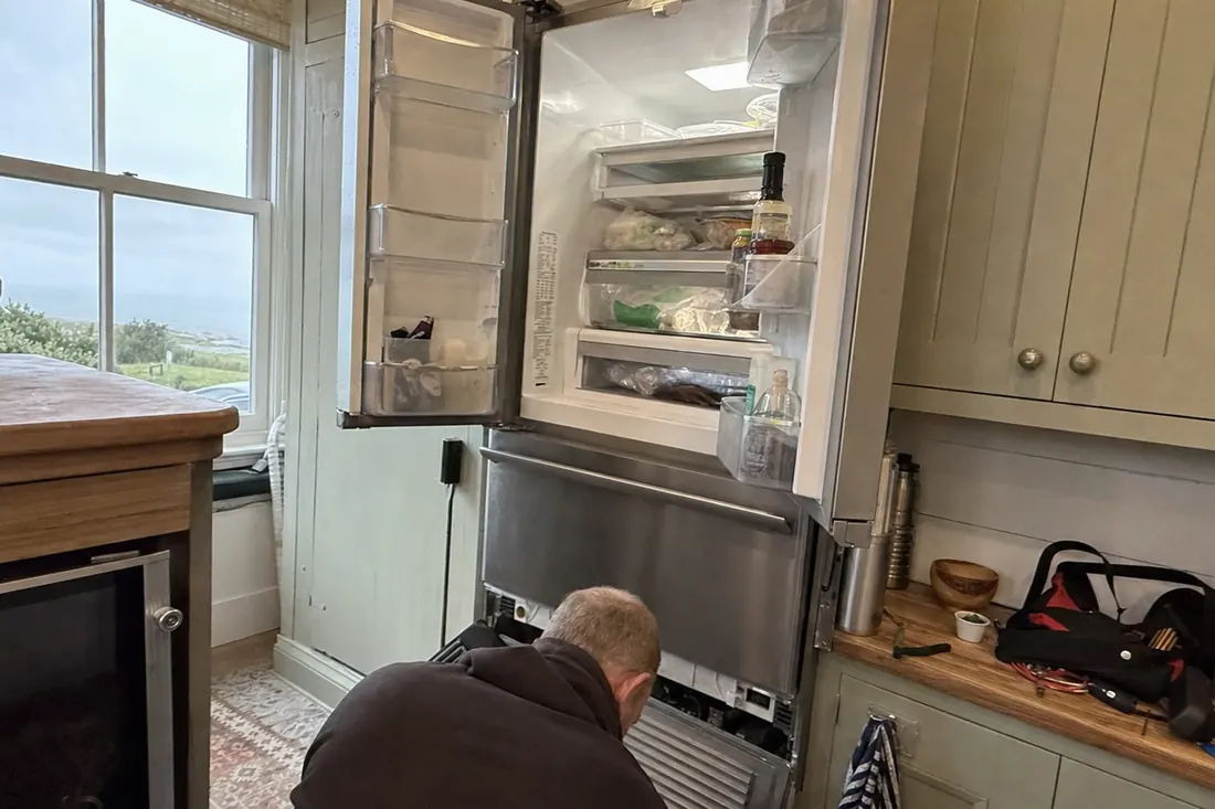 An open built-in refrigerator in a coastal kitchen, technician at the lower grille, the lower grille visible in the picture - Appliance repair at the Beaches
